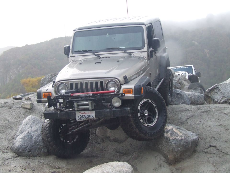 Silver Jeep Wrangler Rubicon with winch and off-road tires climbing rocks