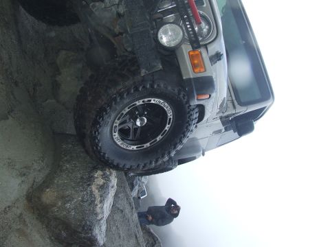 1978 Ford Bronco - A Jeep Wrangler is precariously balanced on rocks, with a person observing from below.