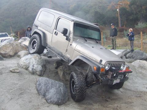 1978 Ford Bronco - A silver Jeep Wrangler navigates a rocky obstacle course with two onlookers nearby.