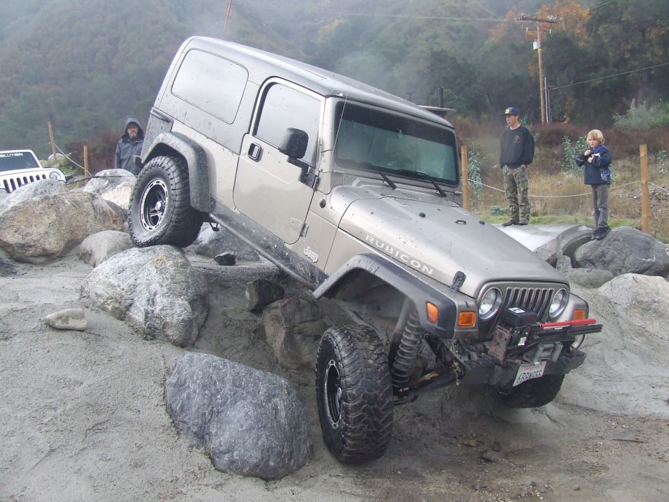 Silver Jeep Wrangler Rubicon off-roading over rocks, front right tire elevated