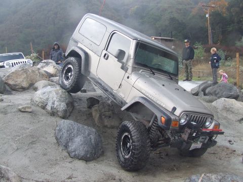 1978 Ford Bronco - A silver Jeep Wrangler Rubicon tackles a challenging rock crawling course, with another Jeep visible in the background.