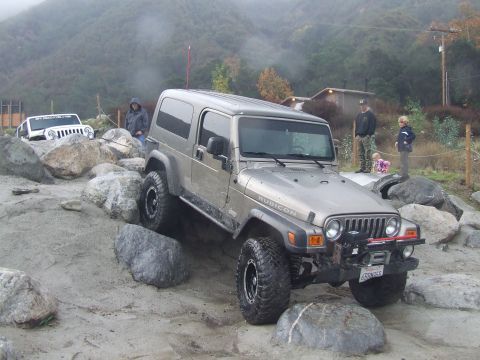 1978 Ford Bronco - Two Jeeps tackle a rocky obstacle course on a cloudy day.