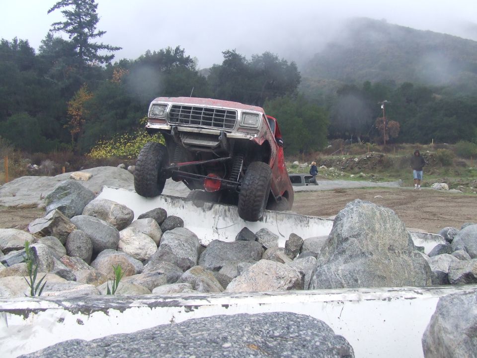 Red 1978 Ford Bronco climbing rocks, front 3/4 view