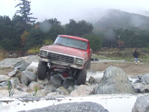 1978 Ford Bronco - A red pickup truck navigates a rocky obstacle course on an overcast day.