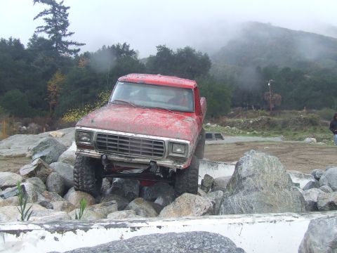 1978 Ford Bronco - A red pickup truck is shown off-road, climbing over large rocks with a misty mountain in the background.