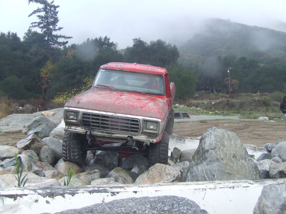 Red pickup truck with a chrome grille and square headlights navigating a rocky obstacle course