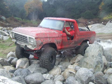 1978 Ford Bronco - A red 1978 Ford Bronco navigates a rocky terrain with a driver behind the wheel.