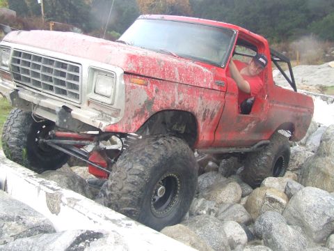 1978 Ford Bronco - A red off-road SUV is shown navigating a rocky terrain with a driver inside.
