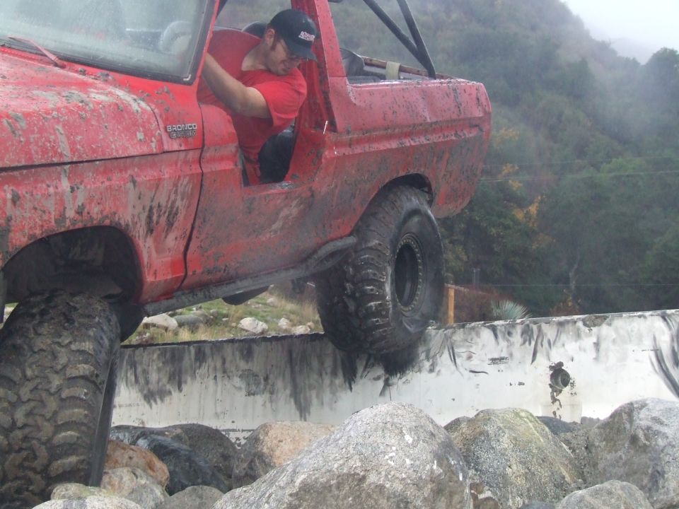 Red 1978 Ford Bronco climbing over rocks, driver visible