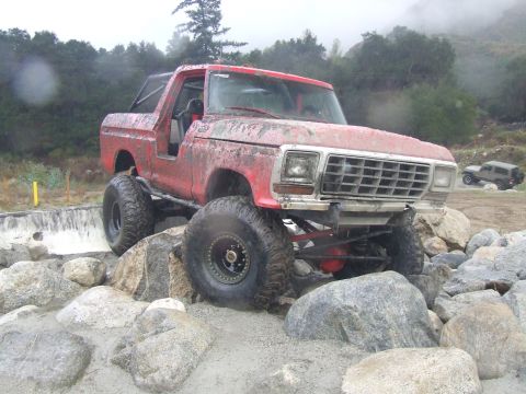 1978 Ford Bronco - A red off-road SUV navigates a rocky terrain, with another vehicle visible in the distance.