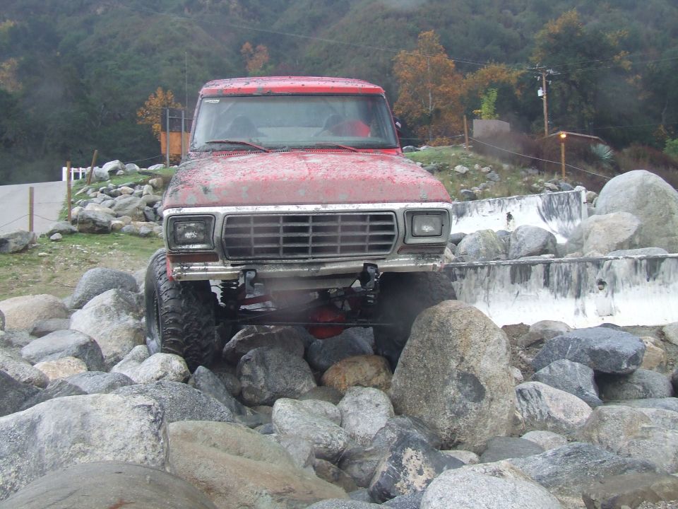 Red 1978 Ford Bronco off-roading over rocks, front view