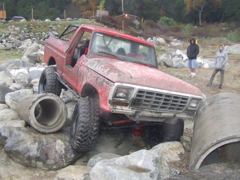 1978 Ford Bronco - A red 1978 Ford Bronco is shown off-roading through a rocky terrain with concrete pipes.
