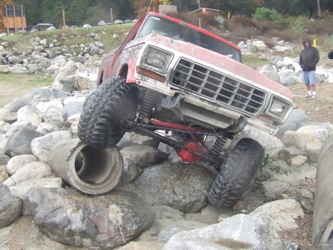 1978 Ford Bronco - This heavily modified truck is attempting to climb over large rocks and a concrete pipe.