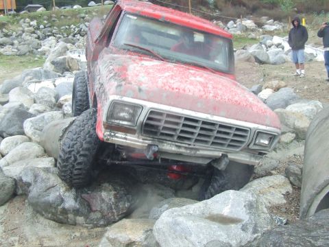 1978 Ford Bronco - A red pickup truck is shown off-roading over large rocks.