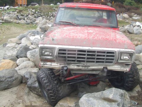 1978 Ford Bronco - This red 1978 Ford Bronco is shown from the front, tackling a challenging rocky obstacle.