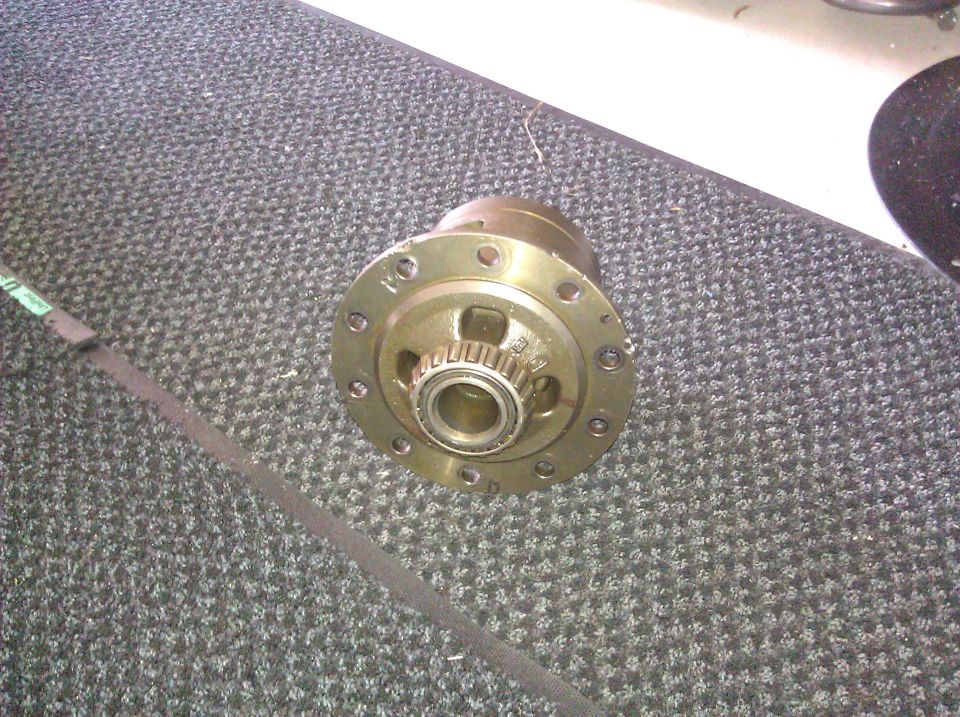 Differential carrier with bearing and gear teeth, on a grey carpeted surface