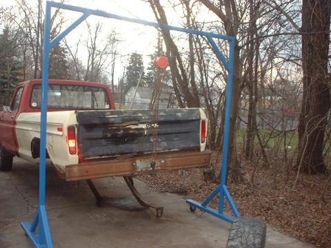 1993 Ford Bronco - The bed of a two-tone red and white pickup truck is suspended by a blue engine hoist, suggesting a repair or restoration in progress.