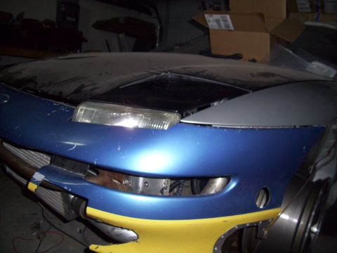 1995 Ford Probe - Car front with blue and yellow paint, visible radiator, and headlight assembly.