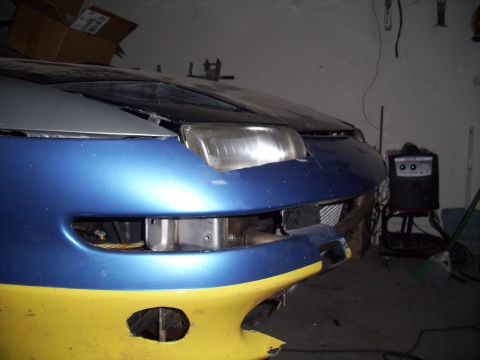 1995 Ford Probe - The front of a two-tone blue and yellow car shows damage to the headlight and bumper area, with visible internal components.