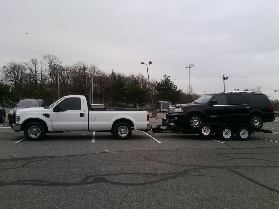 White Ford F-250 Super Duty pickup truck towing a black Lincoln Navigator on a triple-axle trailer