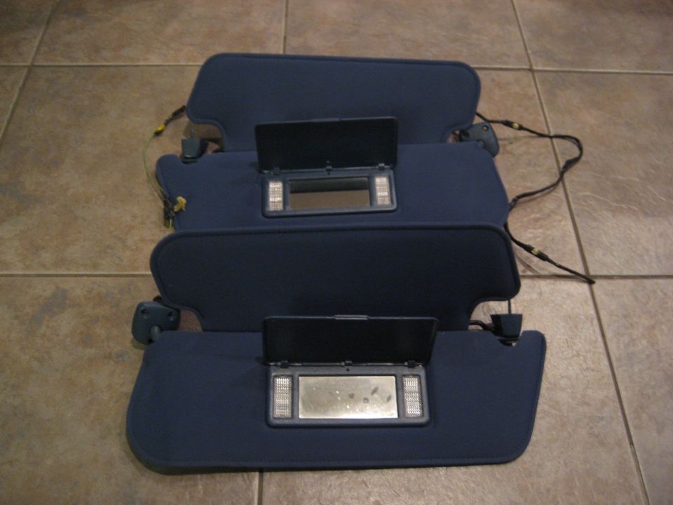 Three blue car sun visors with vanity mirrors and lights, laid out on a tiled floor