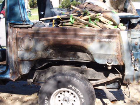 1990 Ford Bronco - The rear section of a heavily rusted vehicle is shown, loaded with lumber and debris.