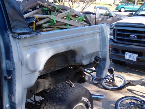 1990 Ford Bronco - A gray Ford truck bed and fender are visible, loaded with wood debris, with another Ford truck parked nearby.