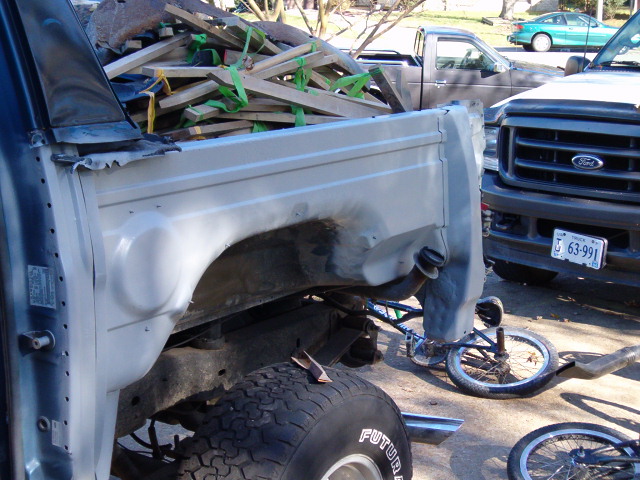 Gray Ford truck bed and fender with wood debris, next to a dark Ford truck