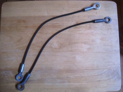 1993 Ford Bronco - Pair of hood release cables with metal eyelet ends, laid on a wooden surface.