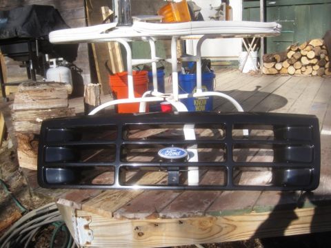 1993 Ford Bronco - A black Ford grille with a blue oval emblem is displayed outdoors on a wooden surface.