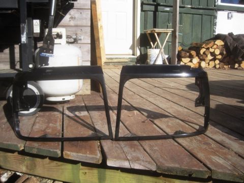 1993 Ford Bronco - Two black headlight bezels are displayed on a wooden deck, with a propane tank and grill visible behind them.