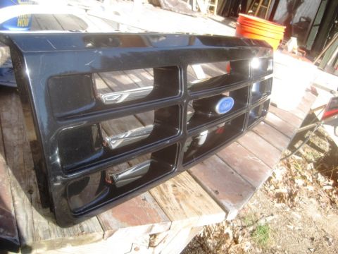 1993 Ford Bronco - A black Ford grille with chrome accents and a blue oval Ford emblem is displayed on a wooden surface.