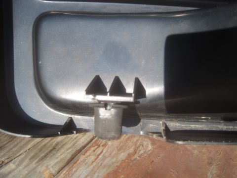 1993 Ford Bronco - A plastic trim clip is shown attached to a gray panel, resting on wooden planks.