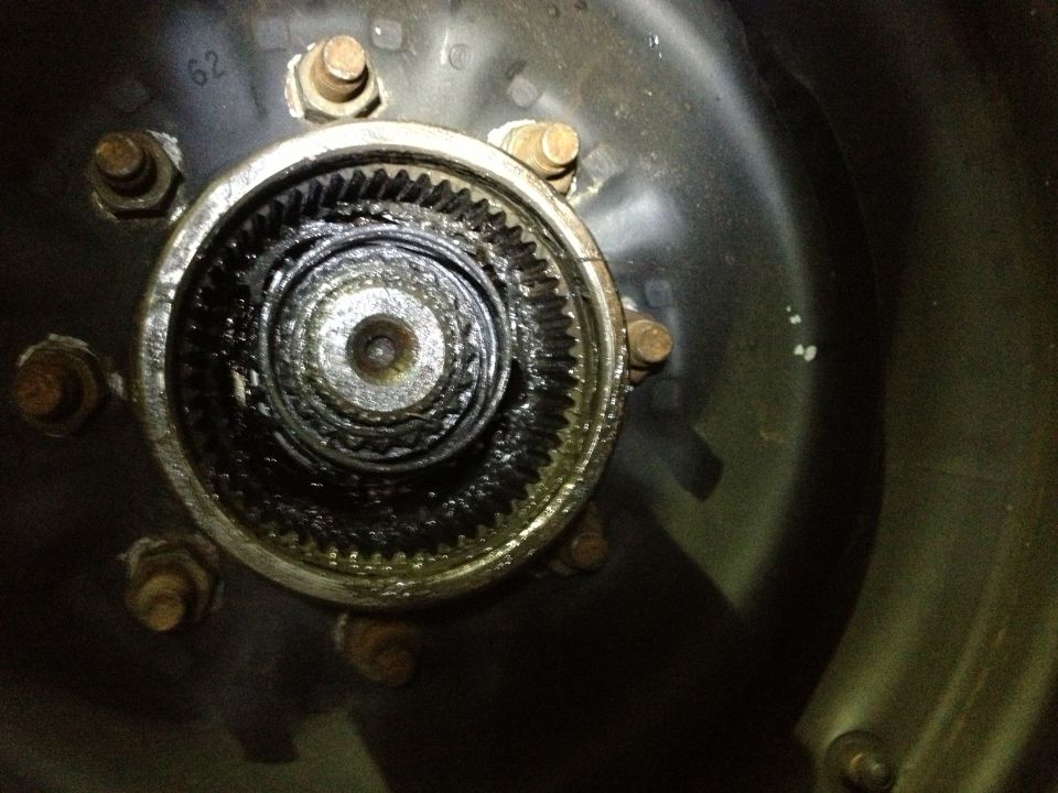 Close-up of a greasy, toothed wheel hub assembly with six lug nuts visible