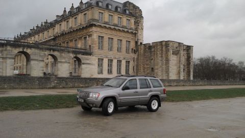 1991 Ford Crown Victoria - A silver Jeep Grand Cherokee is parked on a wet road in front of a large, historic stone building.