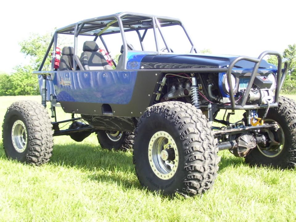 Blue off-road buggy with roll cage, large tires, and exposed engine, viewed from the front-right