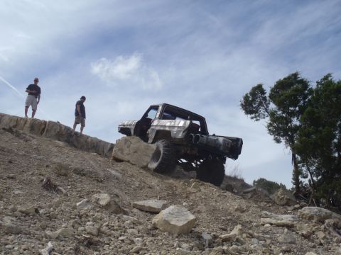 1979 Ford Bronco - A heavily modified truck navigates a challenging rocky terrain under a cloudy sky.
