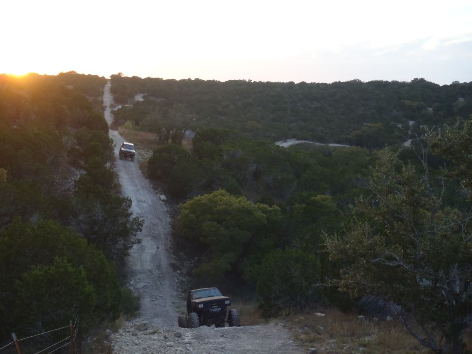 Two off-road vehicles on a dirt road in a wooded area at sunset