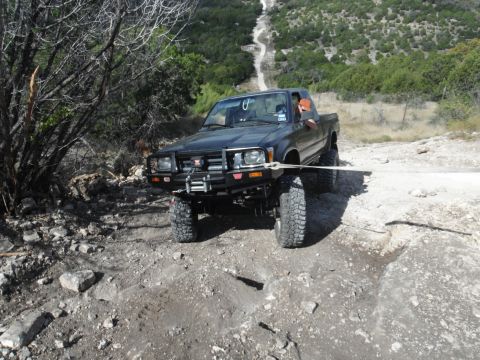 1979 Ford Bronco - A black Toyota pickup truck is being pulled out of a ditch on a rocky, off-road trail.