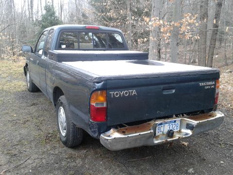 1978 Ford F-150 - A dark blue Toyota Tacoma pickup truck is parked outdoors on a dirt surface with trees in the background.