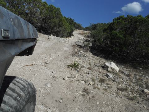 1979 Ford Bronco - Camouflage-painted SUV navigates a challenging rocky trail under a clear blue sky.