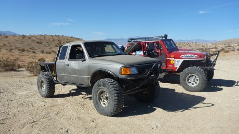 1997 Ford Ranger - Two off-road vehicles are parked in a desert area under a clear blue sky.