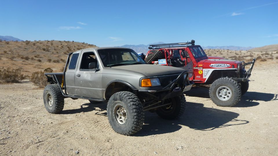 Gray Ford Ranger with big tires parked next to a red Jeep in a desert landscape