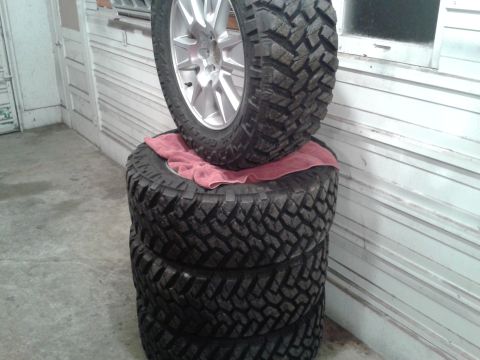 1978 Ford F-150 - A set of four aggressive off-road tires are stacked, with one mounted on a silver alloy wheel.
