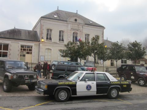 1991 Ford LTD Crown Victoria - A police car with "CANINE PATROL" and "SAFETY AND SERVICE" text is parked outside a building with other vehicles.