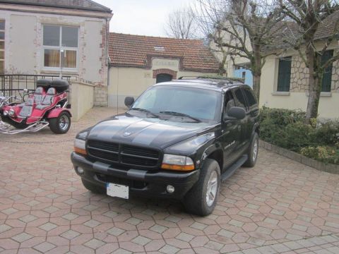 1991 Ford LTD Crown Victoria - Black Dodge Durango with racing stripes parked on a paved driveway next to a red trike.