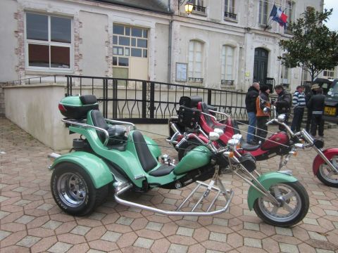 1991 Ford LTD Crown Victoria - A green trike motorcycle is parked on a cobblestone street next to another trike.