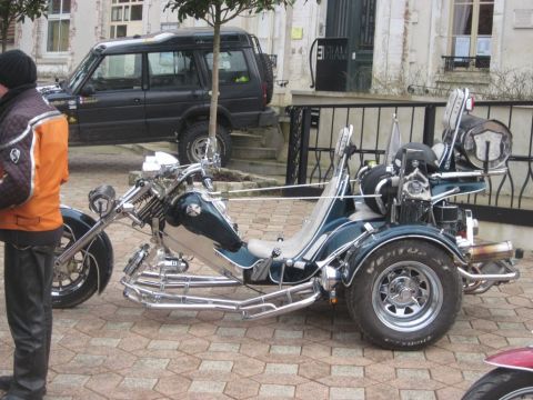 1991 Ford LTD Crown Victoria - A custom trike motorcycle is parked on a brick-paved surface, with a black SUV in the background.