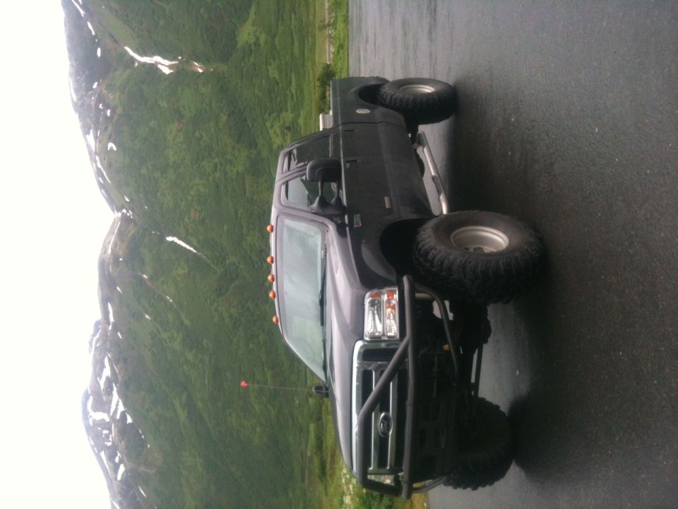 Dark pickup truck with off-road tires and brush guard parked on wet asphalt