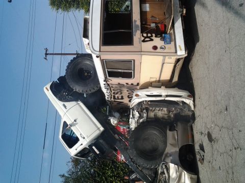 1986 Ford Bronco - An RV has crashed and is lying on its side, crushing a car beneath it.